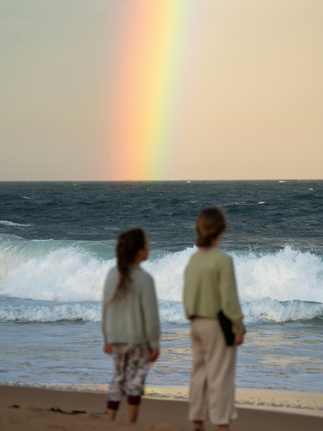 Two kids looking out at the sea and there is a rainbow in the distance