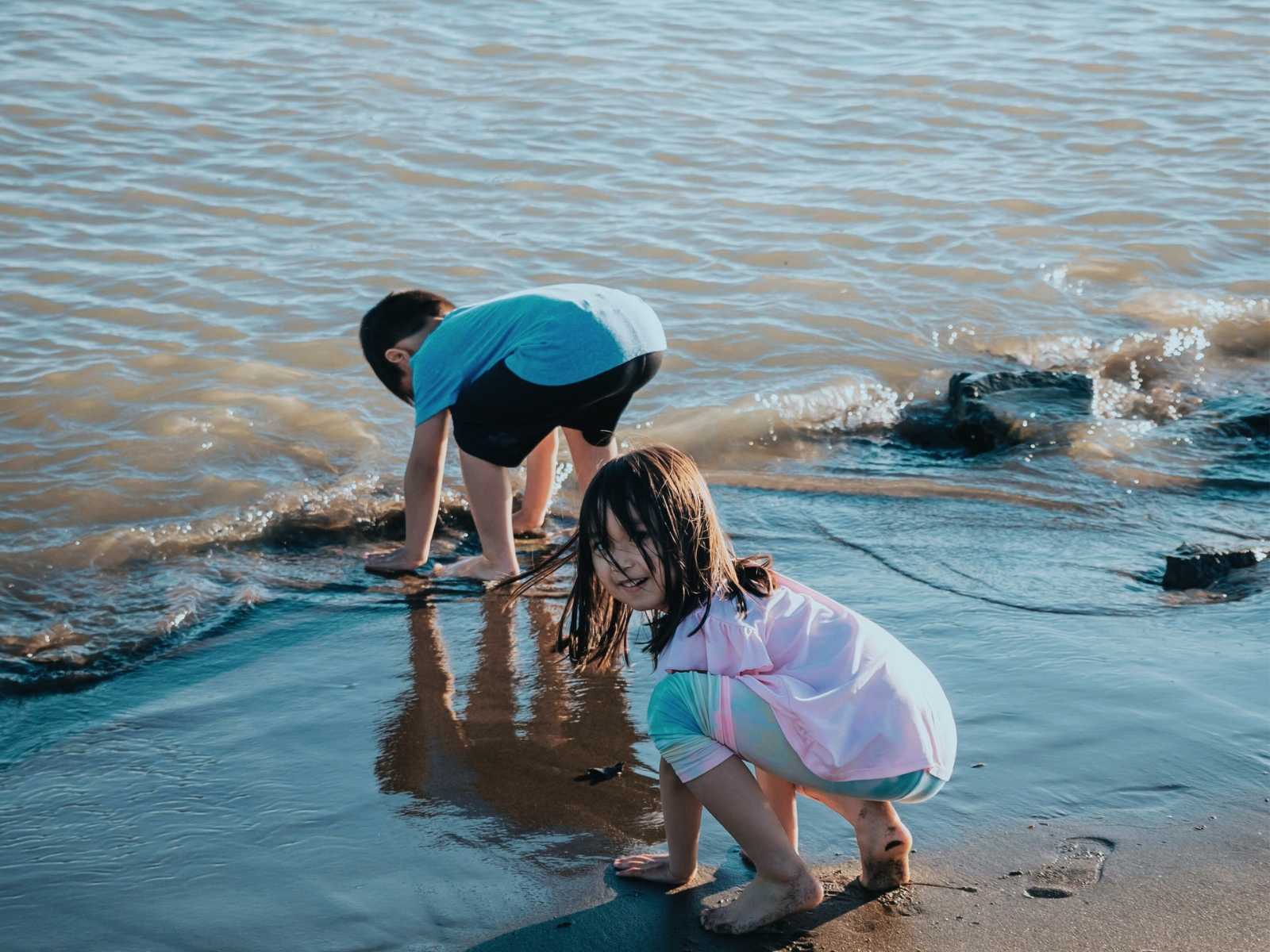 A couple of kids playing in the shallows at the beach.
