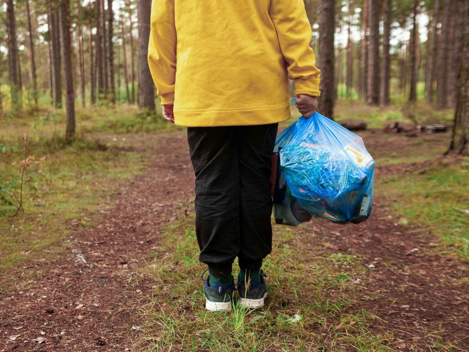 A kid holding a bag of rubbish in a forest