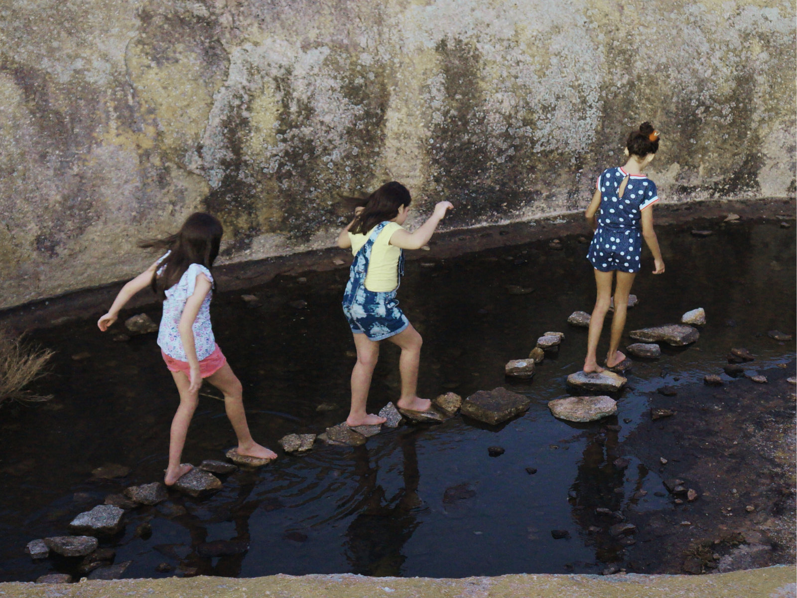 Three kids walking across stepping stones.
